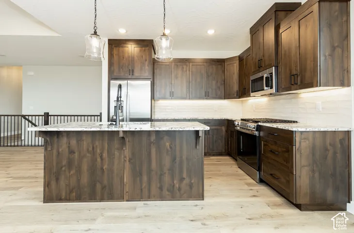 Kitchen featuring dark wood-finish cabinetry, stainless steel appliances, light-toned countertops, and a full tile backsplash