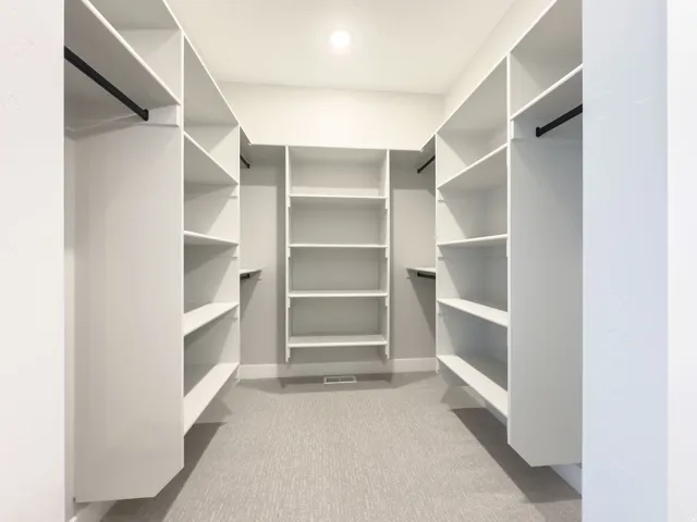 Spacious walk-in closet featuring extensive built-in shelving, multiple hanging rods, and a neutral carpeted floor