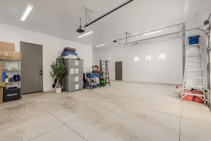 Spacious garage with light-colored concrete flooring, multiple recessed light fixtures, and two grey-paneled doors
