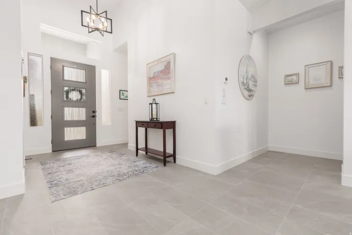 Spacious entryway featuring a contemporary gray door with frosted glass panels, two tall side windows, and a modern geometric chandelier
