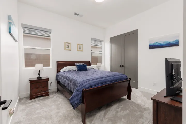 Carpeted bedroom featuring white walls, dual windows with blinds, and a double-door closet with dark hardware