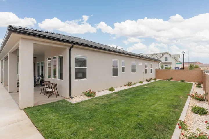 Rear exterior featuring a covered patio, stucco siding, and a fenced yard with manicured lawn and decorative gravel beds