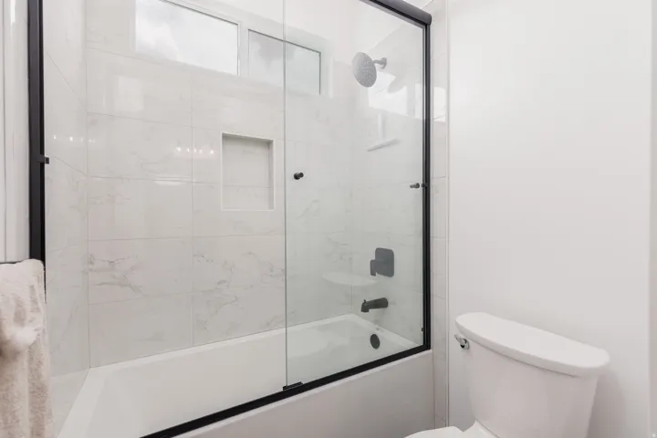 Bathtub-shower combination featuring white tile surround, a built-in shower niche, and a rain showerhead