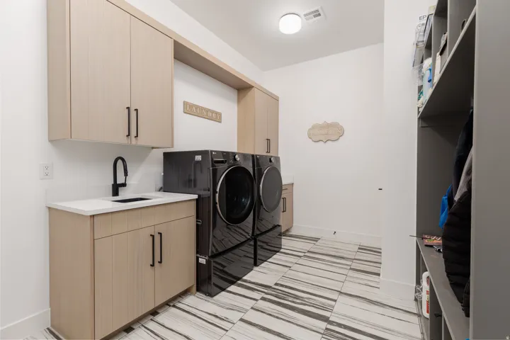 Dedicated laundry room featuring light wood-finish cabinetry, a white countertop with an undermount sink, and a matte black faucet