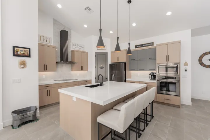Modern kitchen featuring a large central island with seating, light-toned cabinetry, stainless steel appliances, and sleek pendant lighting