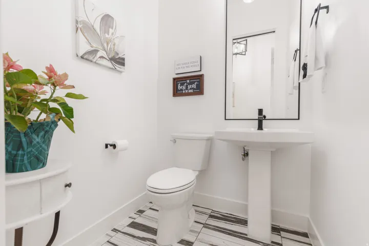 Pedestal sink with a matte black faucet, framed mirror, and striped tile flooring