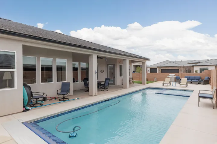 Expansive backyard featuring a rectangular swimming pool with integrated spa, a large covered patio, and concrete decking