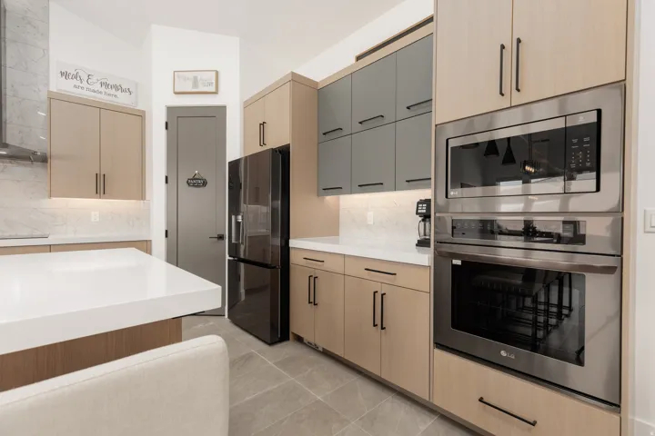 Kitchen featuring a large central island with a white countertop, two-tone cabinetry, integrated stainless steel appliances, a black refrigerator, and a built-in oven and microwave