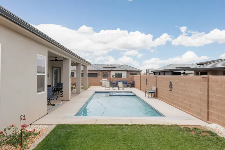 Private backyard featuring a rectangular swimming pool with integrated steps, concrete pool decking, and a low-maintenance grass area