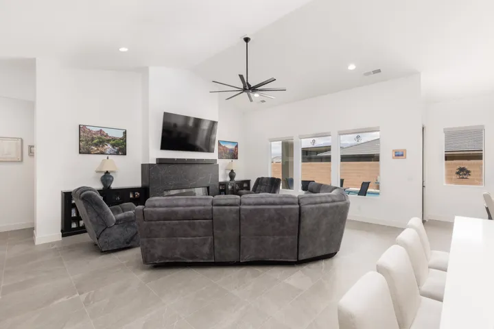 Expansive living area featuring vaulted ceilings with a ceiling fan, large format tile flooring, and a contemporary fireplace with a dark stone surround
