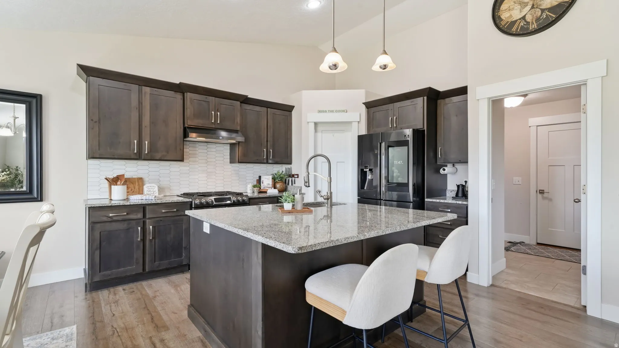 Kitchen featuring dark wood-finish cabinetry, granite countertops, a center island with sink and bar seating, stainless steel appliances, and wood-finish flooring