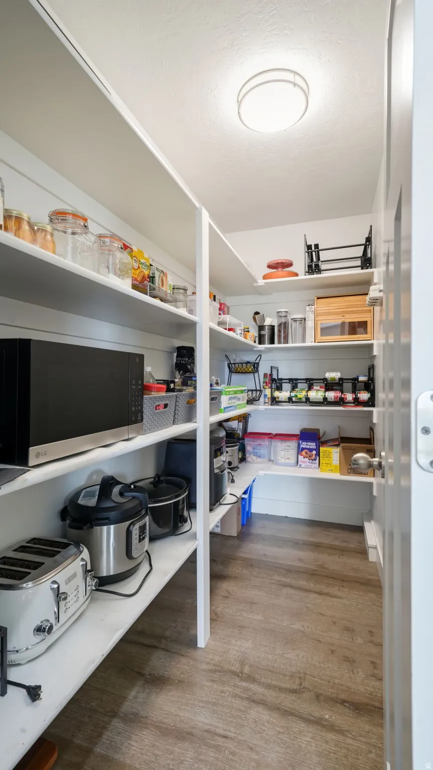 Walk-in pantry featuring white built-in shelving, wood-finish flooring, and a flush-mount ceiling light
