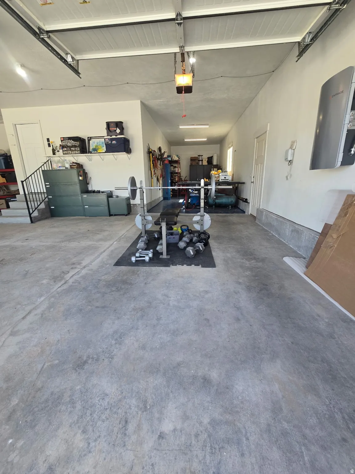 Spacious garage with a concrete floor, overhead garage door system, recessed lighting, and an internal staircase with a black metal railing
