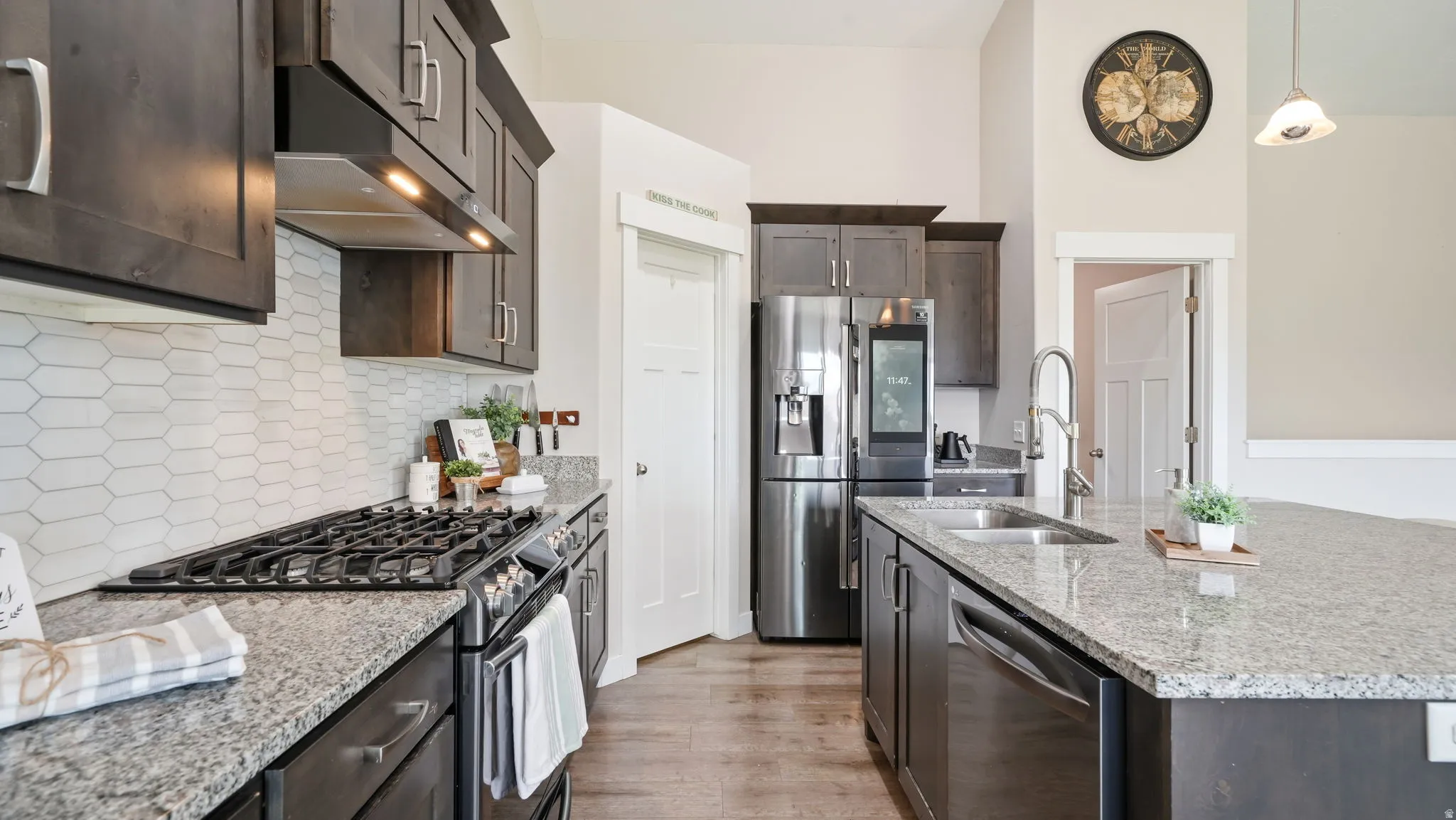 Kitchen featuring dark wood-finish cabinetry, granite countertops, a tile backsplash, wood-finish flooring, and a stainless steel appliances