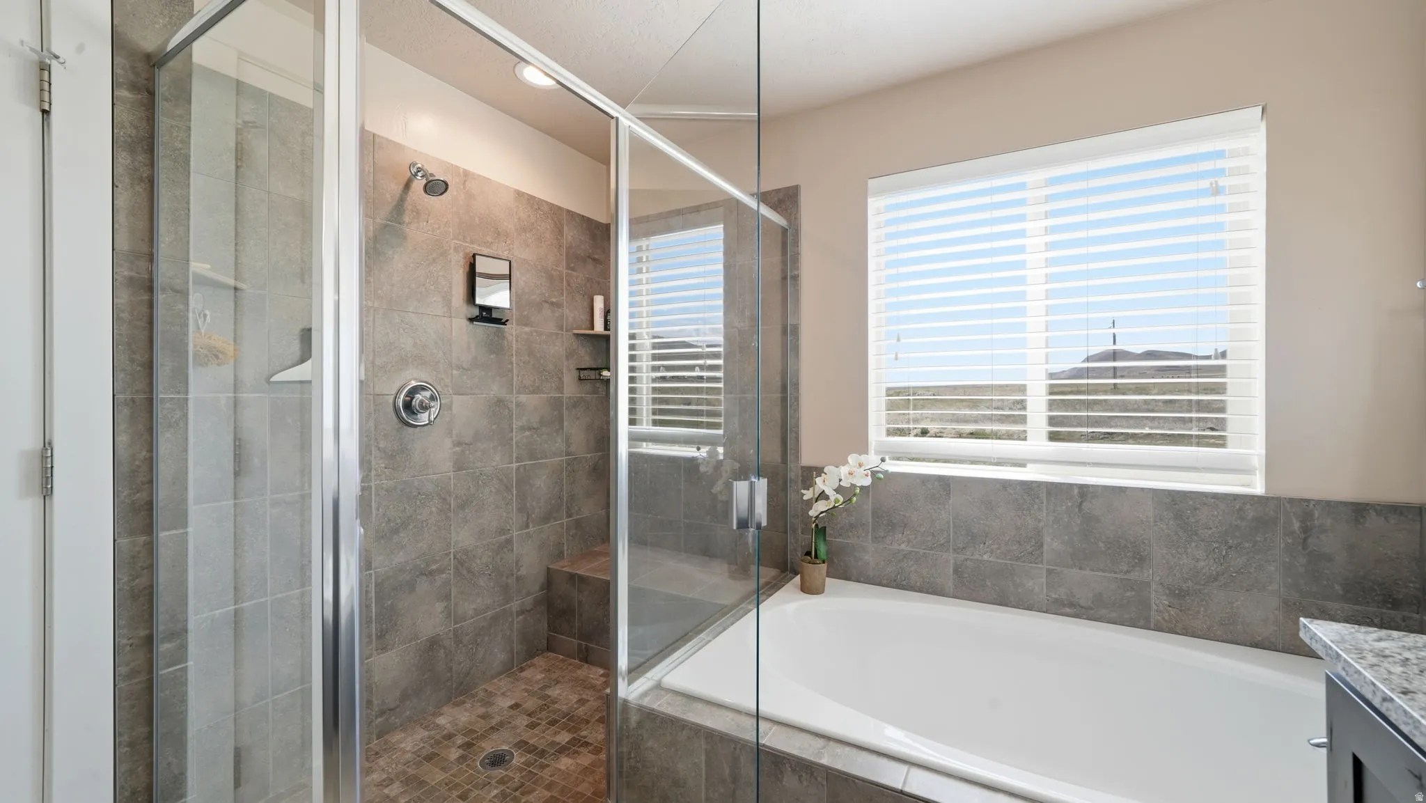 Glass-enclosed shower with stone tile walls, built-in bench, and large soaking tub