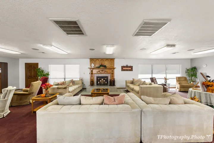 Spacious common area featuring a central fireplace with an ornate wood mantel, multiple windows with roller shades, recessed lighting, and ceiling-mounted air returns