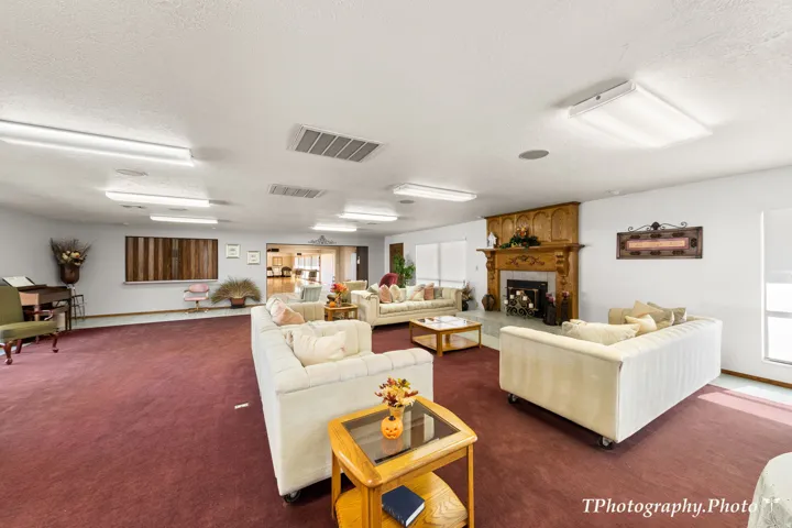 Spacious common area featuring a rich red carpet, multiple windows, and a prominent fireplace with an ornate wood mantel