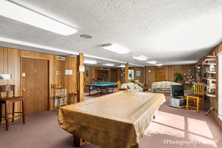Spacious recreation area featuring wood paneling, recessed fluorescent lighting, and carpeting