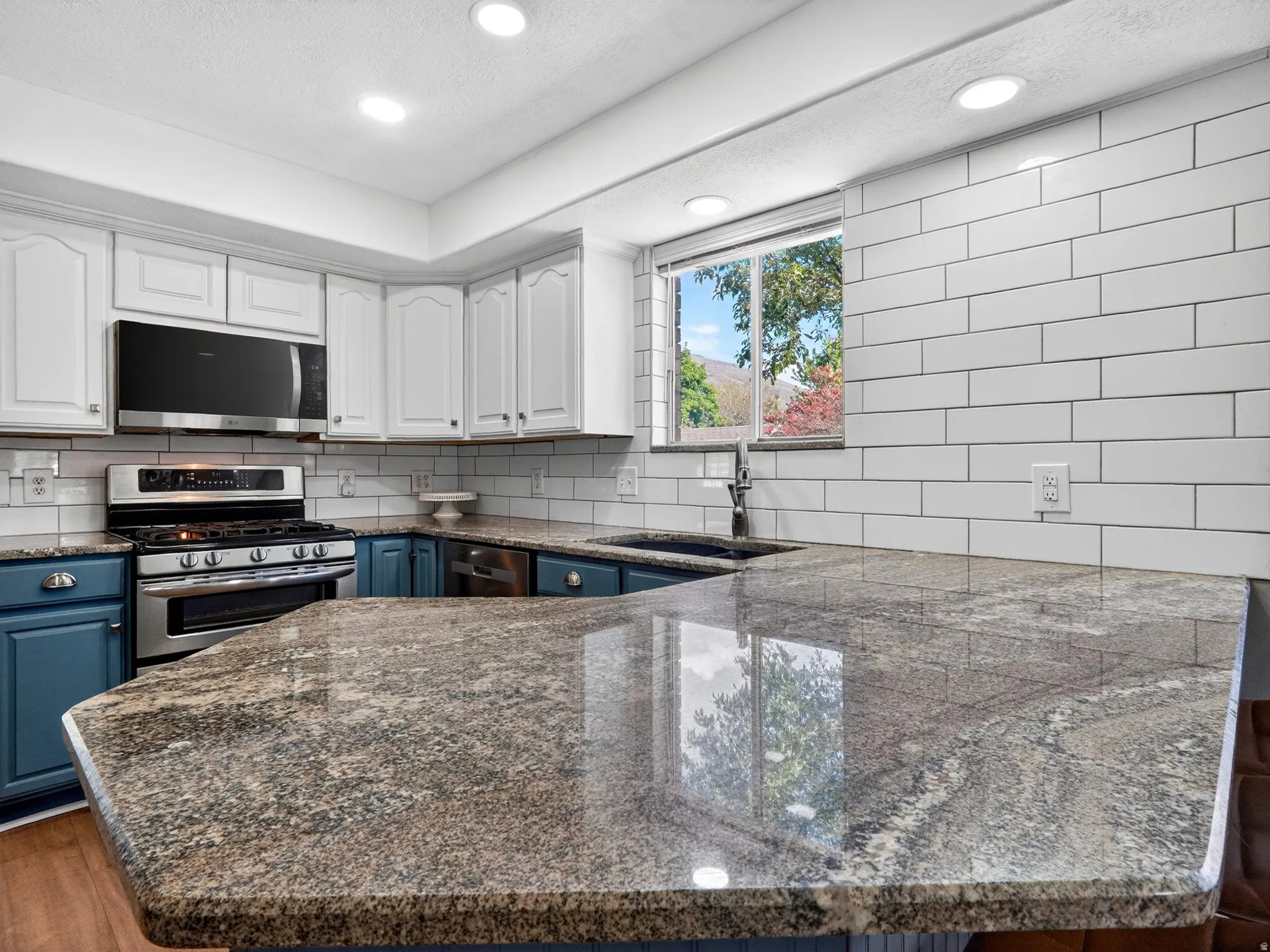 Kitchen featuring granite countertops, white subway tile backsplash, stainless steel appliances, upper white cabinetry, and lower blue cabinetry