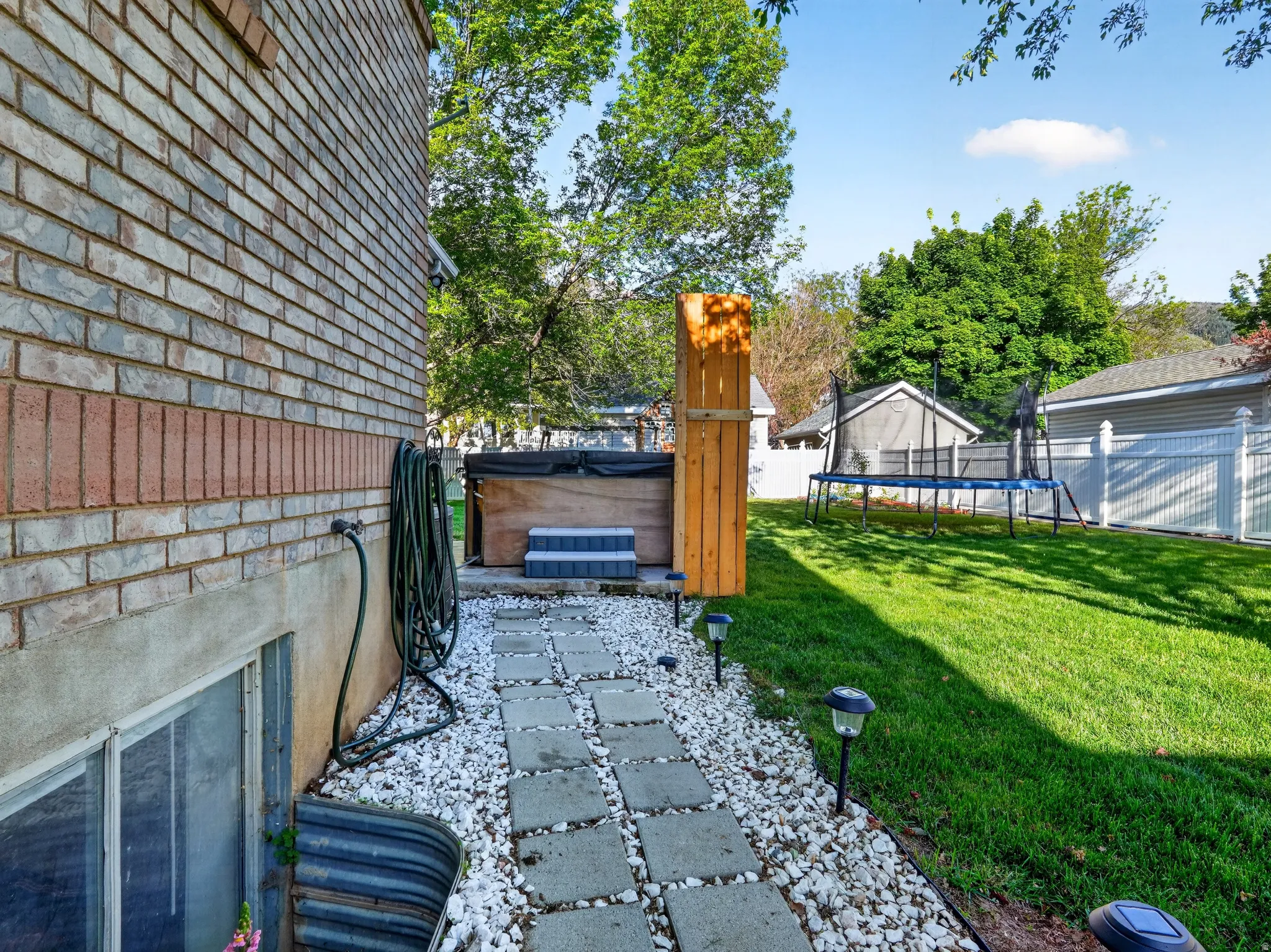 Expansive backyard featuring a lush lawn, white privacy fencing, and a concrete paver pathway with white gravel