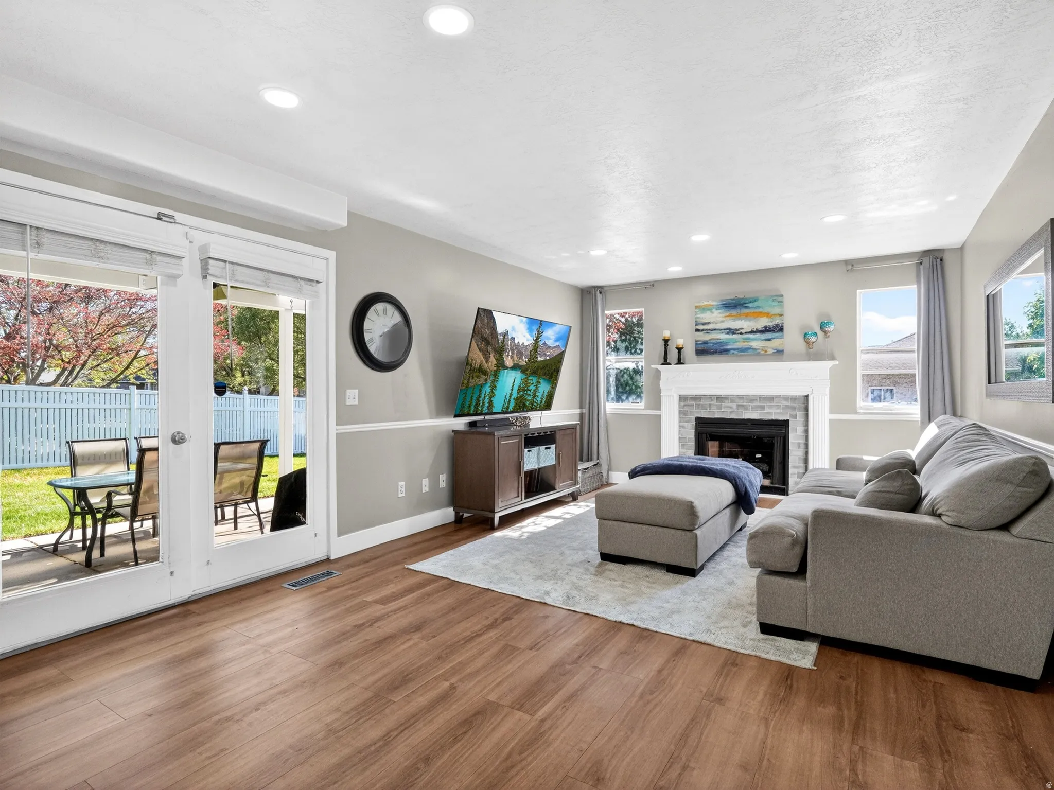 Spacious living area featuring wood-finish flooring, a white mantel fireplace with a brick surround, and recessed ceiling lighting