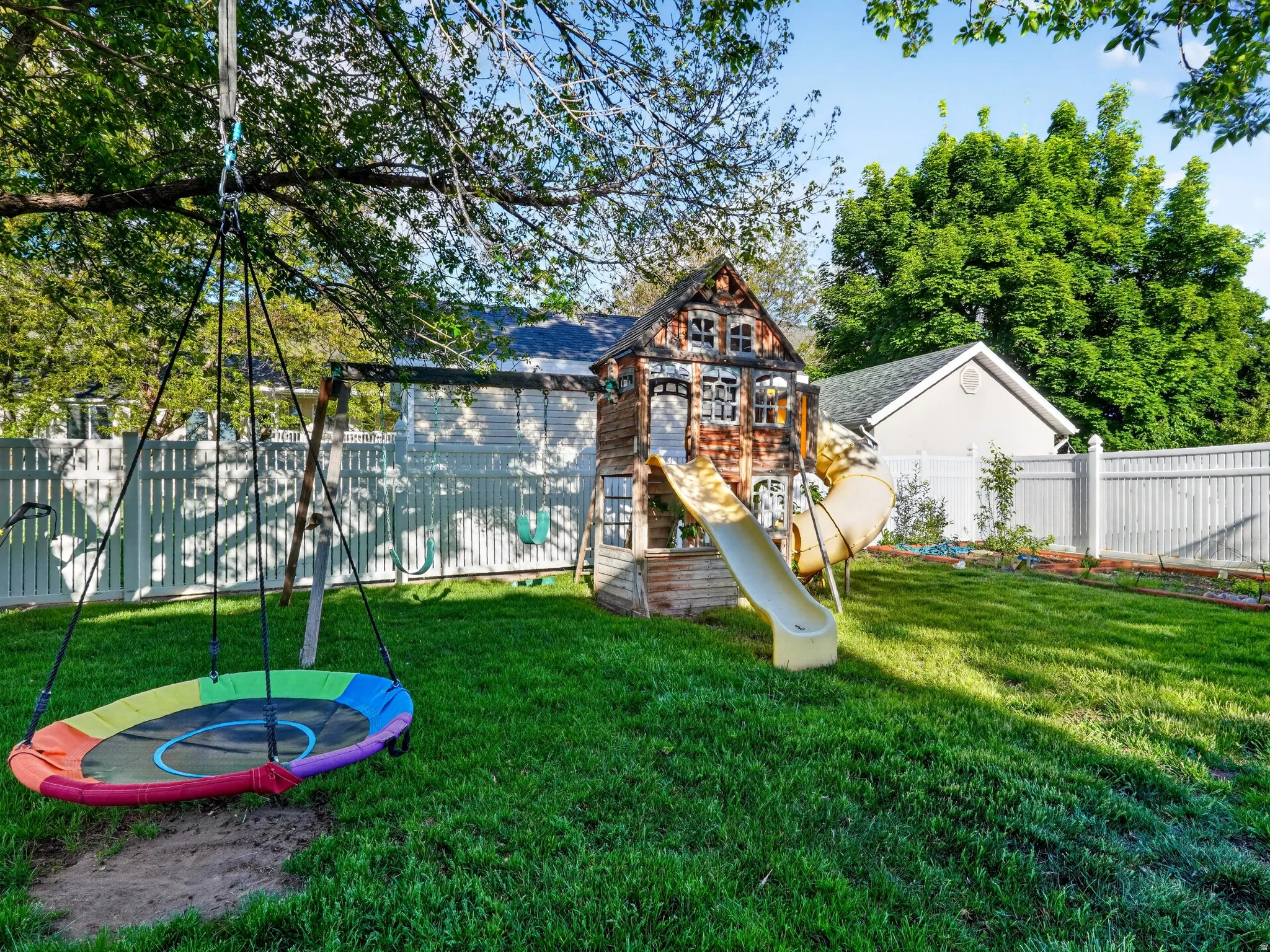 Expansive backyard featuring a lush lawn, white privacy fencing, mature trees, and a detached structure with a gabled roofline