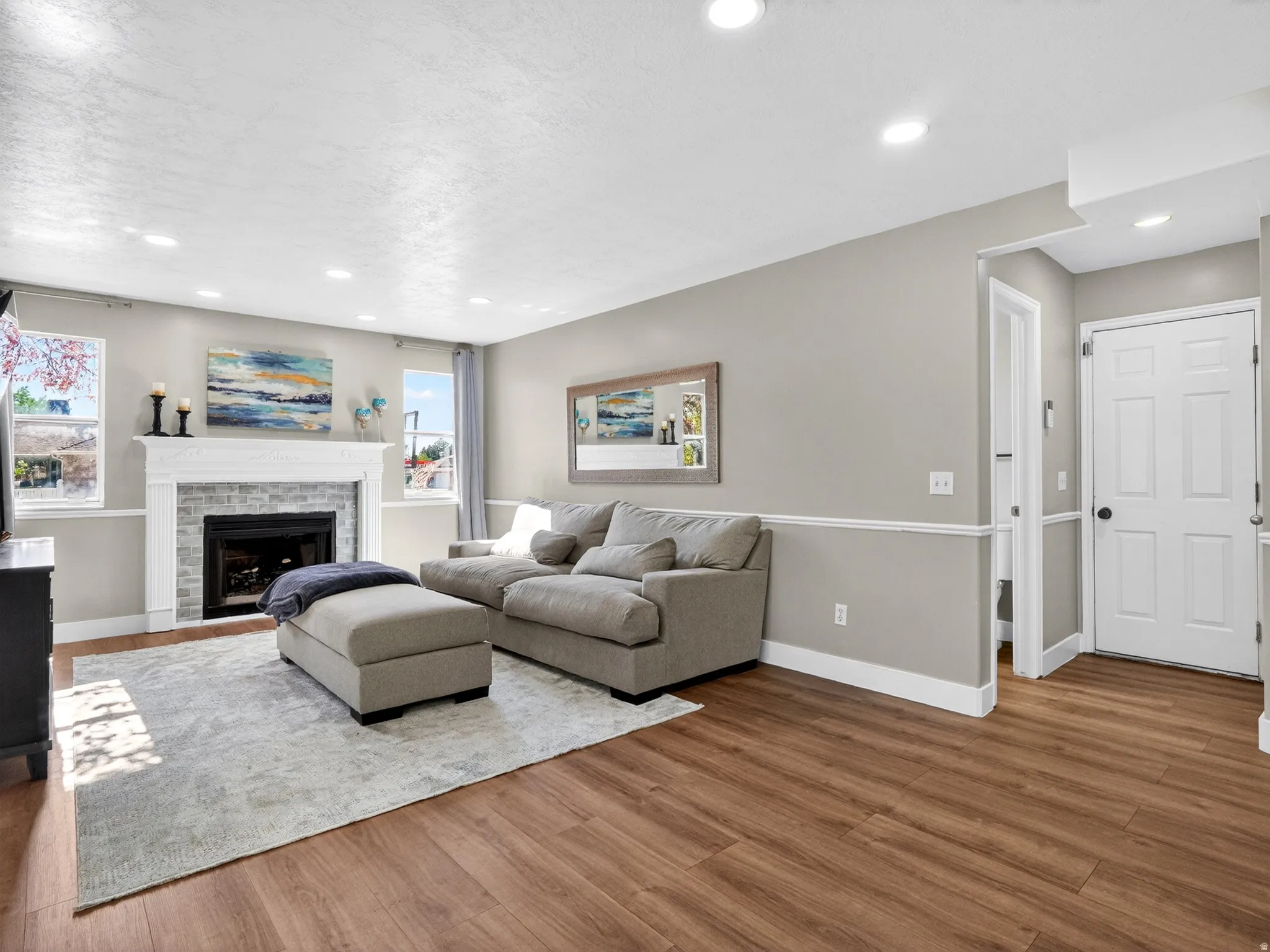 Living area featuring wood-finish flooring, a fireplace with a stone surround and white mantel, recessed lighting, and a white paneled door