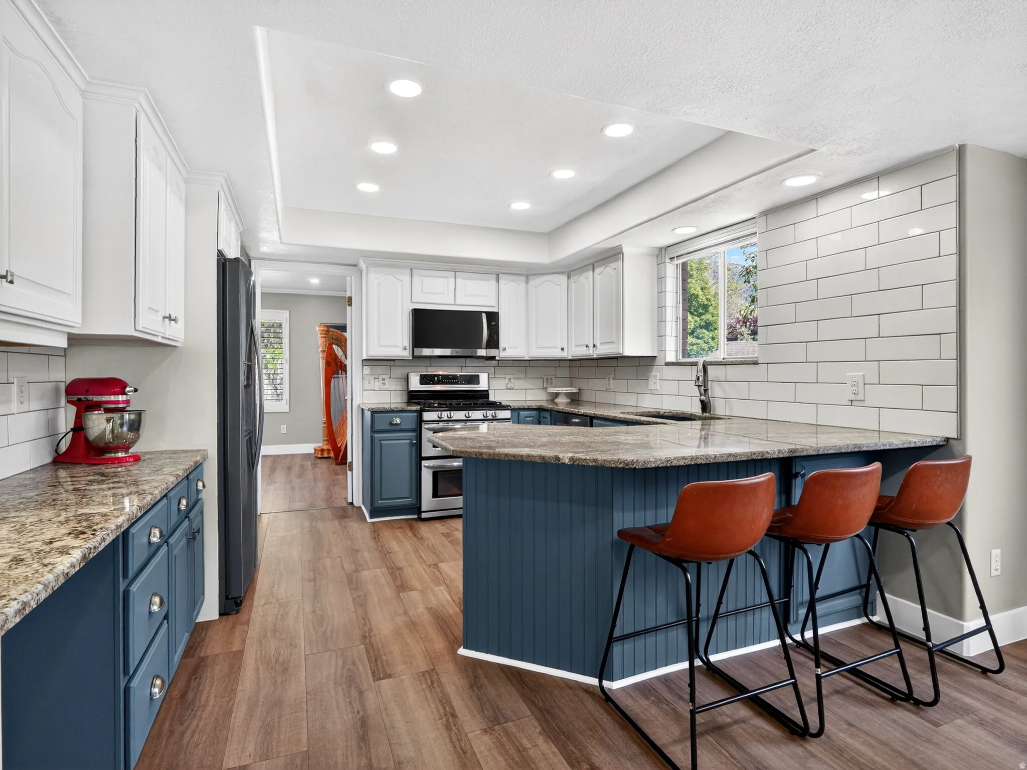 Spacious kitchen featuring a large island with beadboard paneling, two-tone cabinetry, wood-finish flooring, recessed lighting, and a white subway tile backsplash