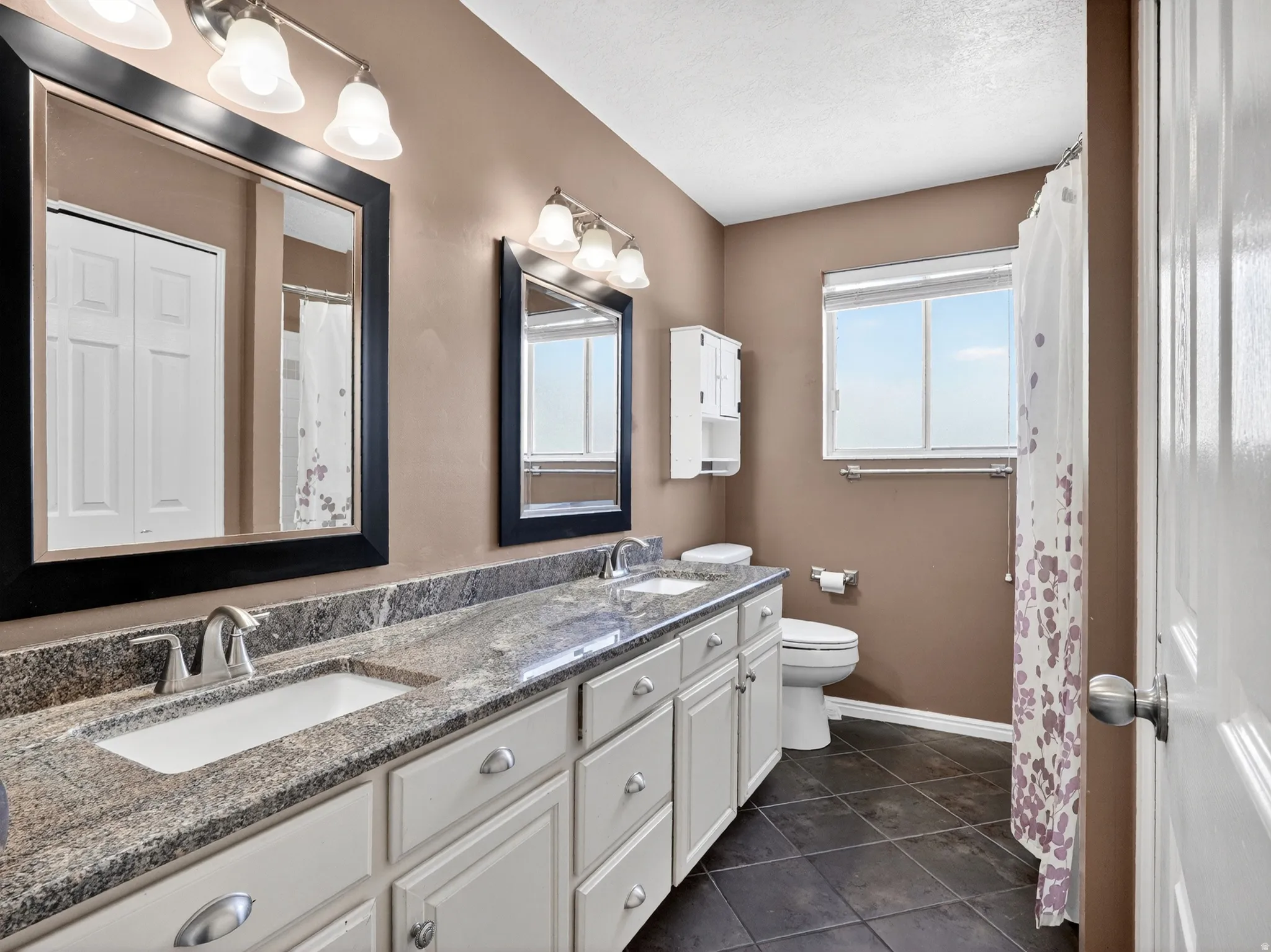 Bathroom featuring a dual vanity with granite-style countertops, white cabinetry with silver hardware, and integrated rectangular sinks