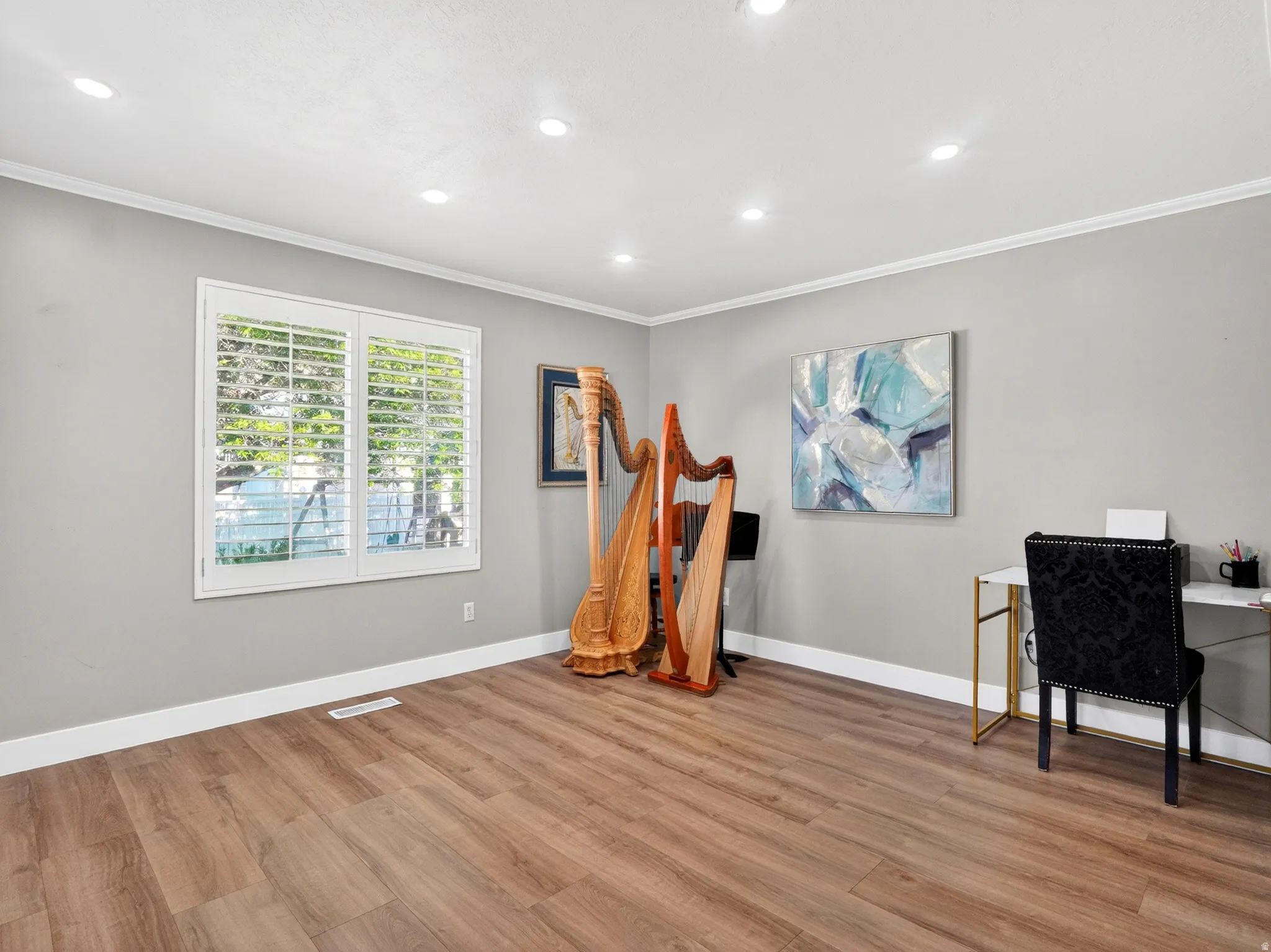 Spacious room featuring wood-finish flooring, recessed lighting, crown molding, and a double window with plantation shutters