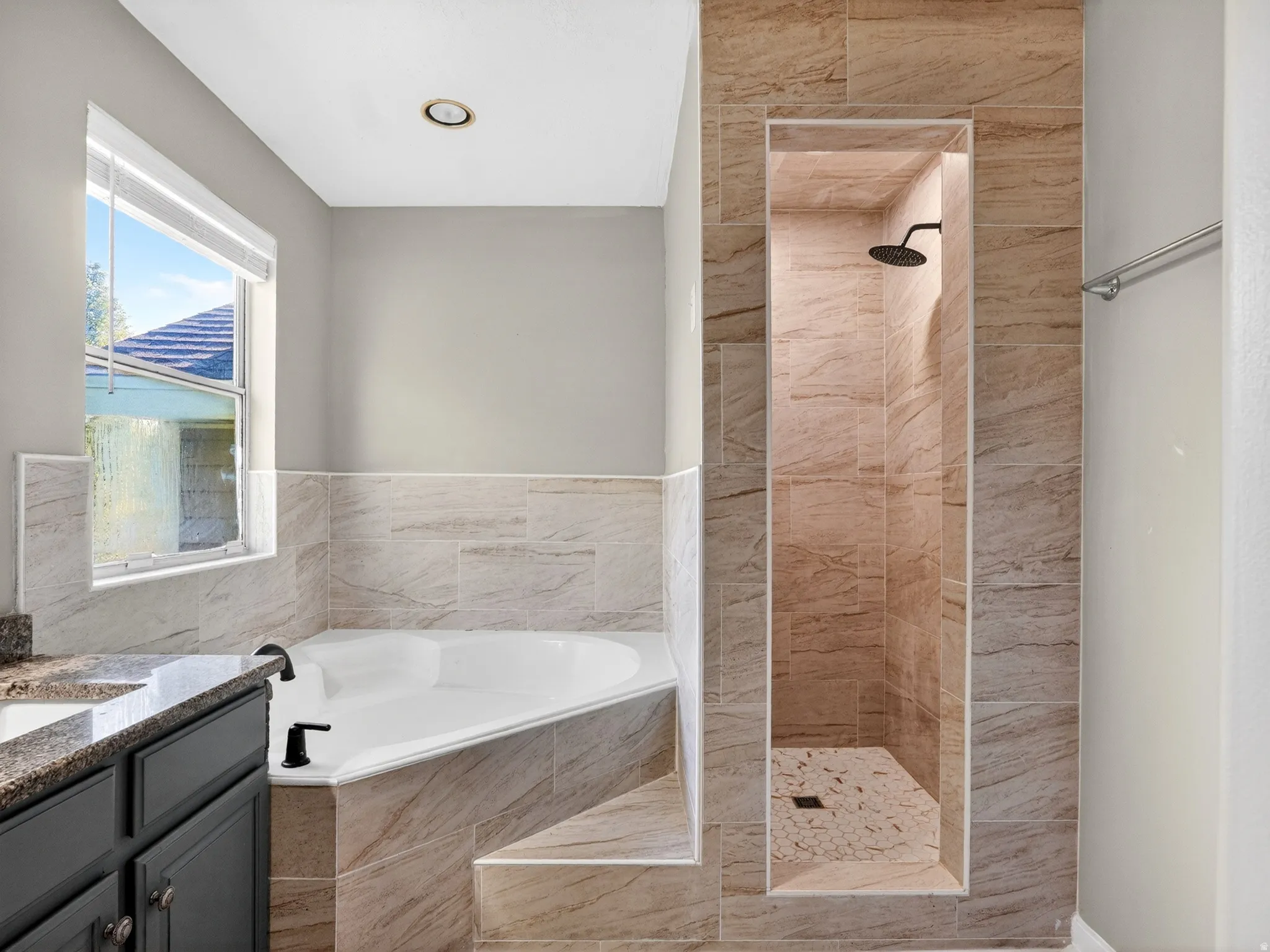 Full bathroom featuring a walk-in shower with a mosaic tile floor, a soaking tub, and a vanity with a dark countertop