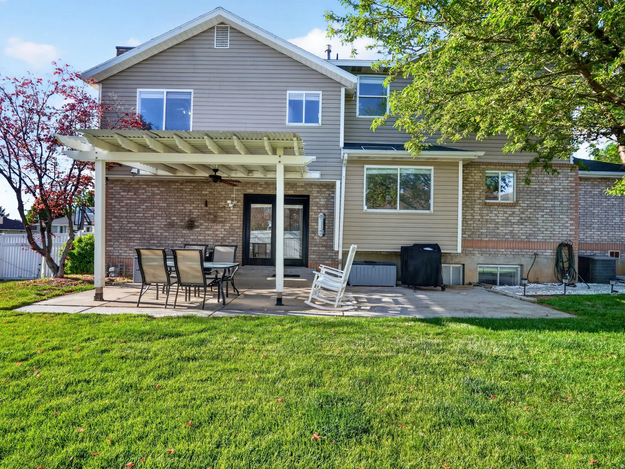 Spacious backyard featuring a concrete patio, a pergola with an attached ceiling fan, and a manicured lawn
