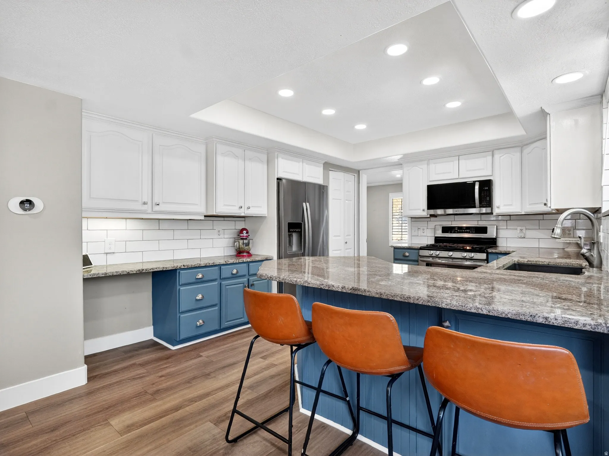 Modern kitchen featuring wood-finish flooring, recessed lighting, white upper cabinetry, a subway tile backsplash, and an island with a built-in sink and stone countertop