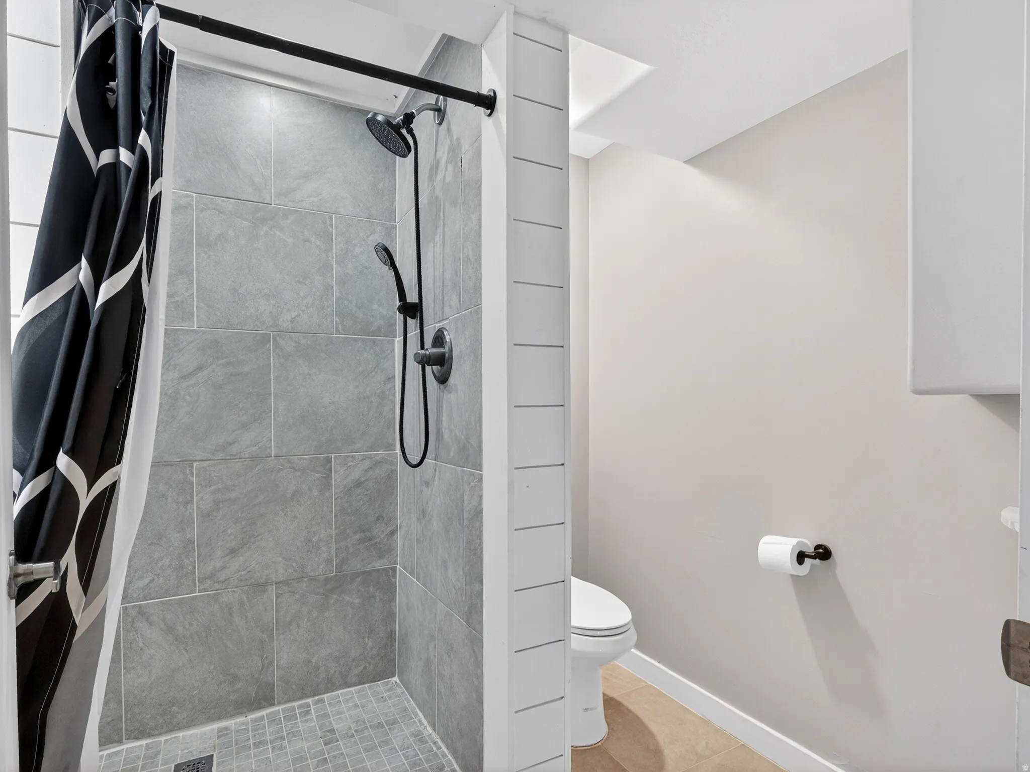 Shower enclosure featuring full-height stone-look tile, a mosaic tile floor, and a matte black shower system with a handheld sprayer