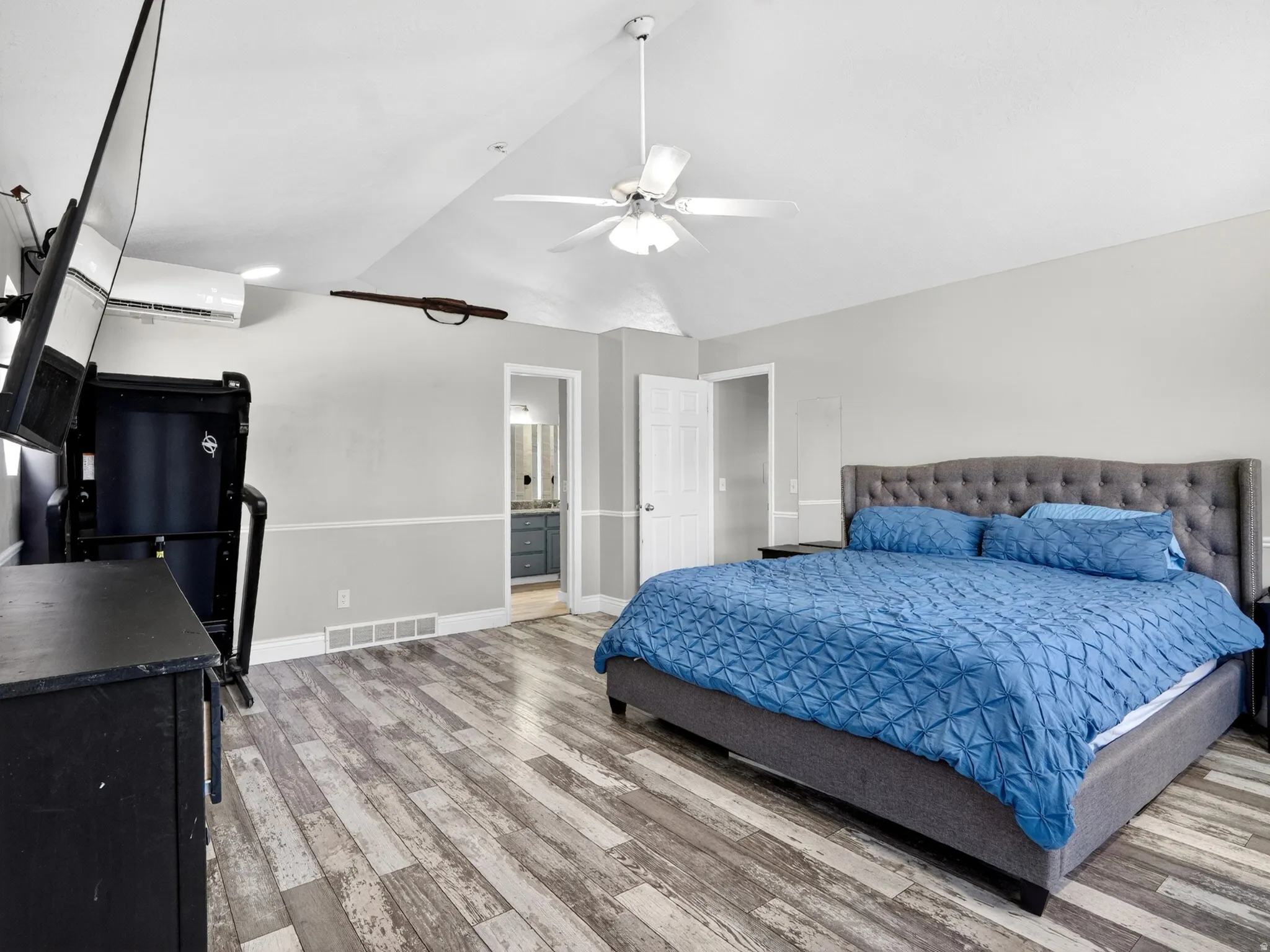Spacious room featuring wood-finish flooring, a vaulted ceiling with a ceiling fan, and a light gray wall color with white trim