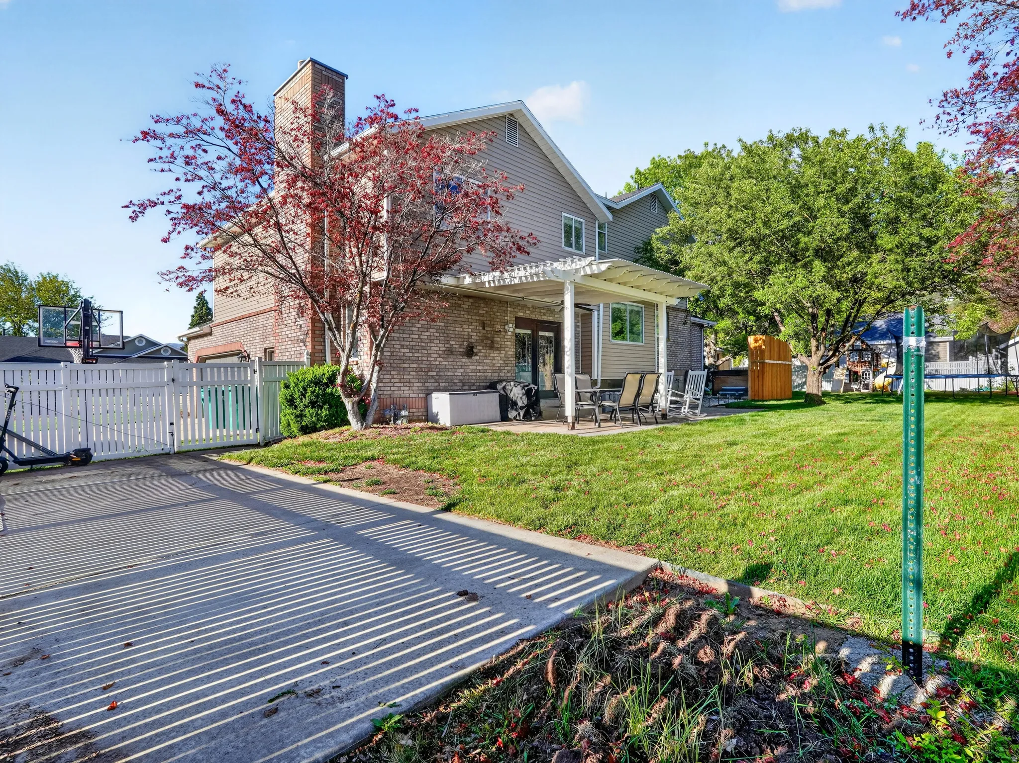 Expansive rear yard featuring a manicured lawn, established landscaping, and a covered patio area
