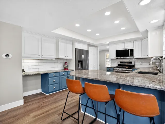 Modern kitchen featuring wood-finish flooring, recessed lighting, white upper cabinetry, a subway tile backsplash, and an island with a built-in sink and stone countertop