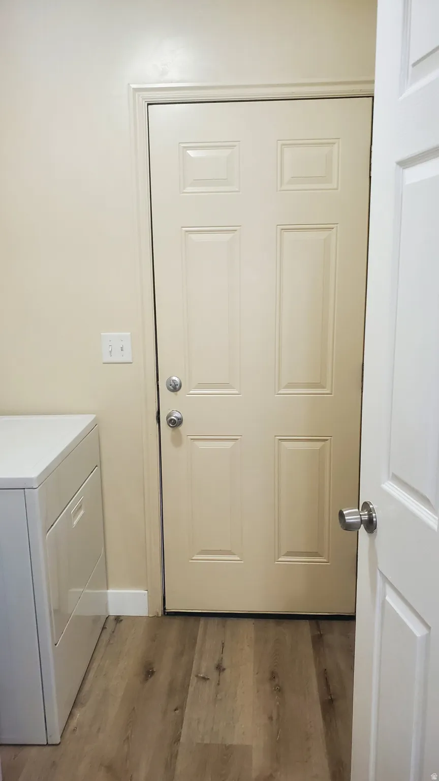 Laundry area with wood-finish flooring, light-toned walls, and a paneled entry door