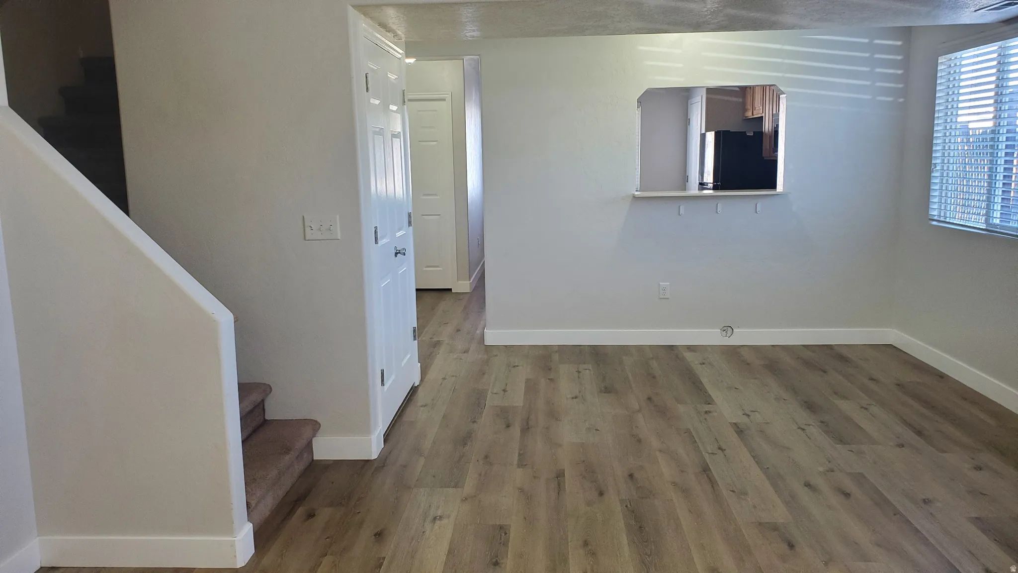 Living area featuring wood-finish flooring, a pass-through window with a ledge, and a window with horizontal blinds