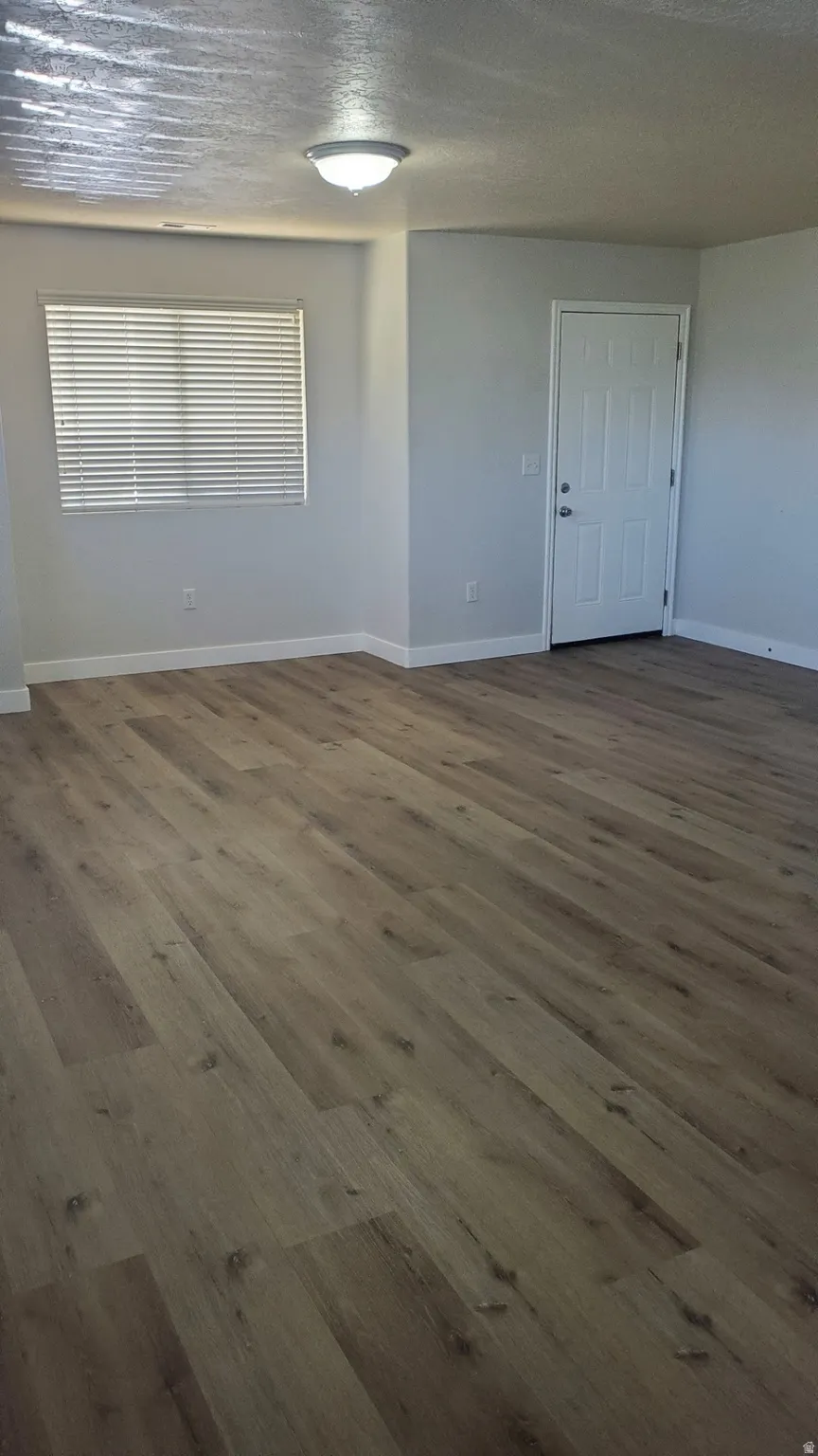 Spacious interior featuring wood-finish flooring, neutral wall tones, a contemporary ceiling light fixture, and a window with horizontal blinds