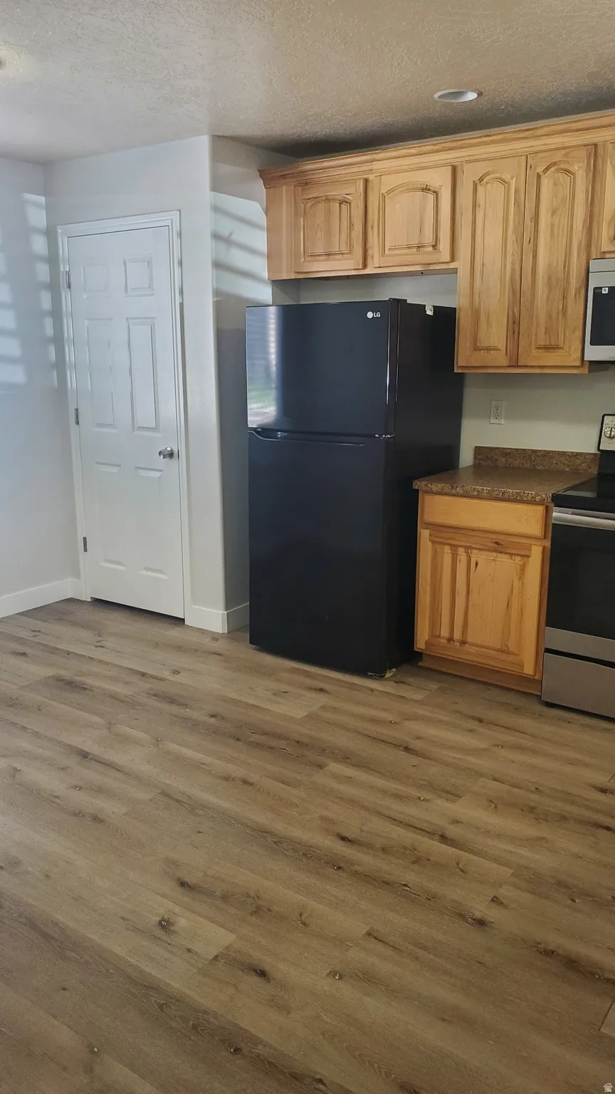 Kitchen area featuring wood-finish flooring, natural wood cabinetry, and a black refrigerator