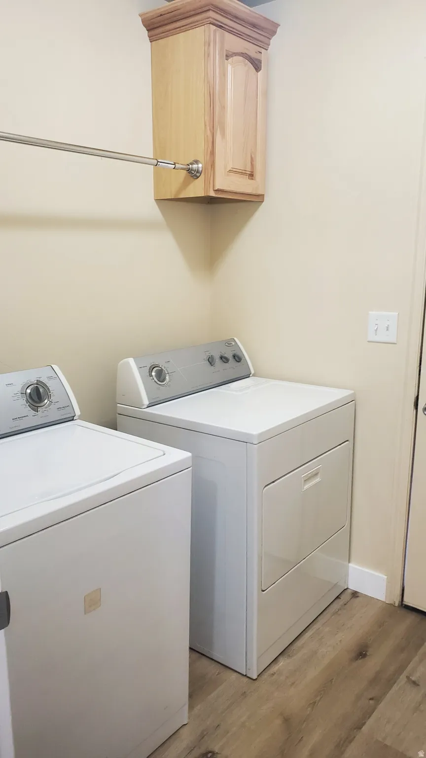Laundry area featuring wood-finish flooring, a wall-mounted light wood cabinet with crown molding, and a chrome hanging rod