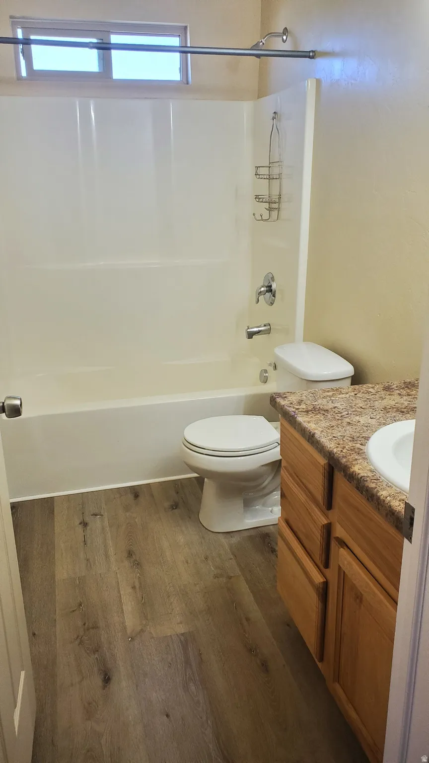 Bathroom featuring a shower-tub combination, wood-finish flooring, a vanity with a patterned countertop, and a window for natural light