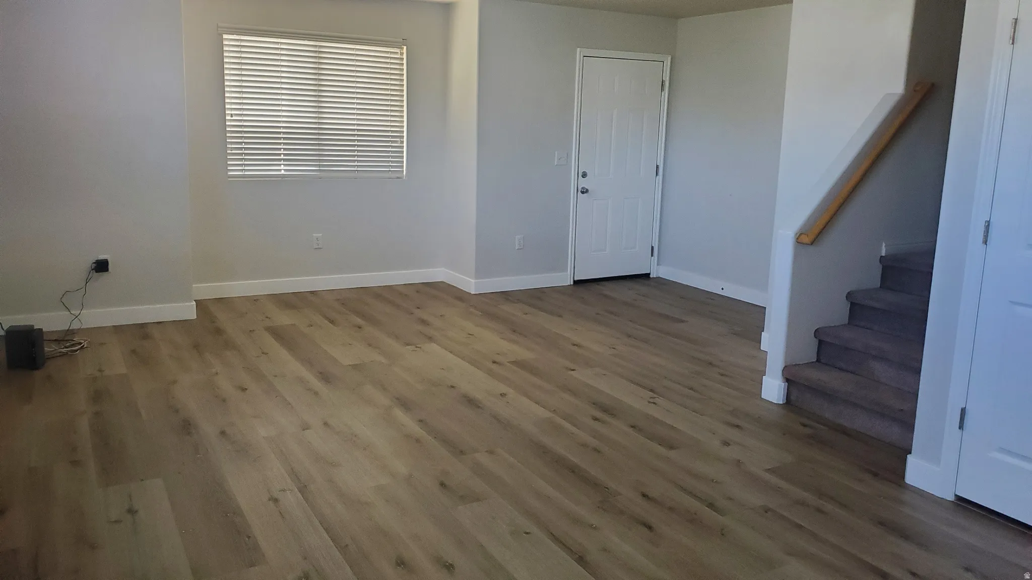 Spacious interior featuring wood-finish flooring, neutral paint, white trim, and a staircase with carpeted treads and a wooden handrail