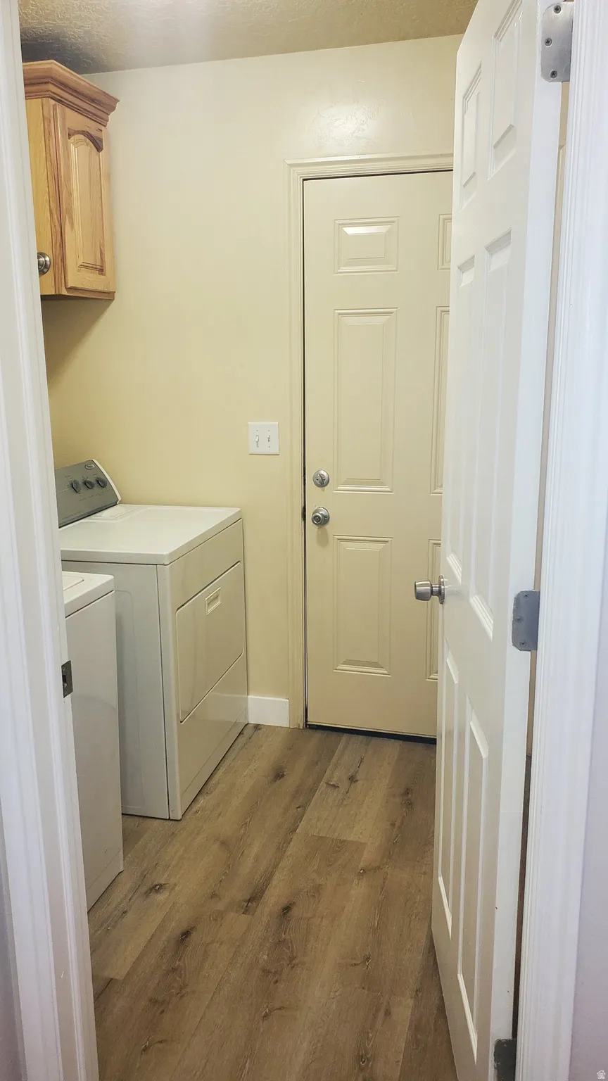 Utility room featuring wood-finish flooring, light-toned walls, and a built-in wood-finish cabinet