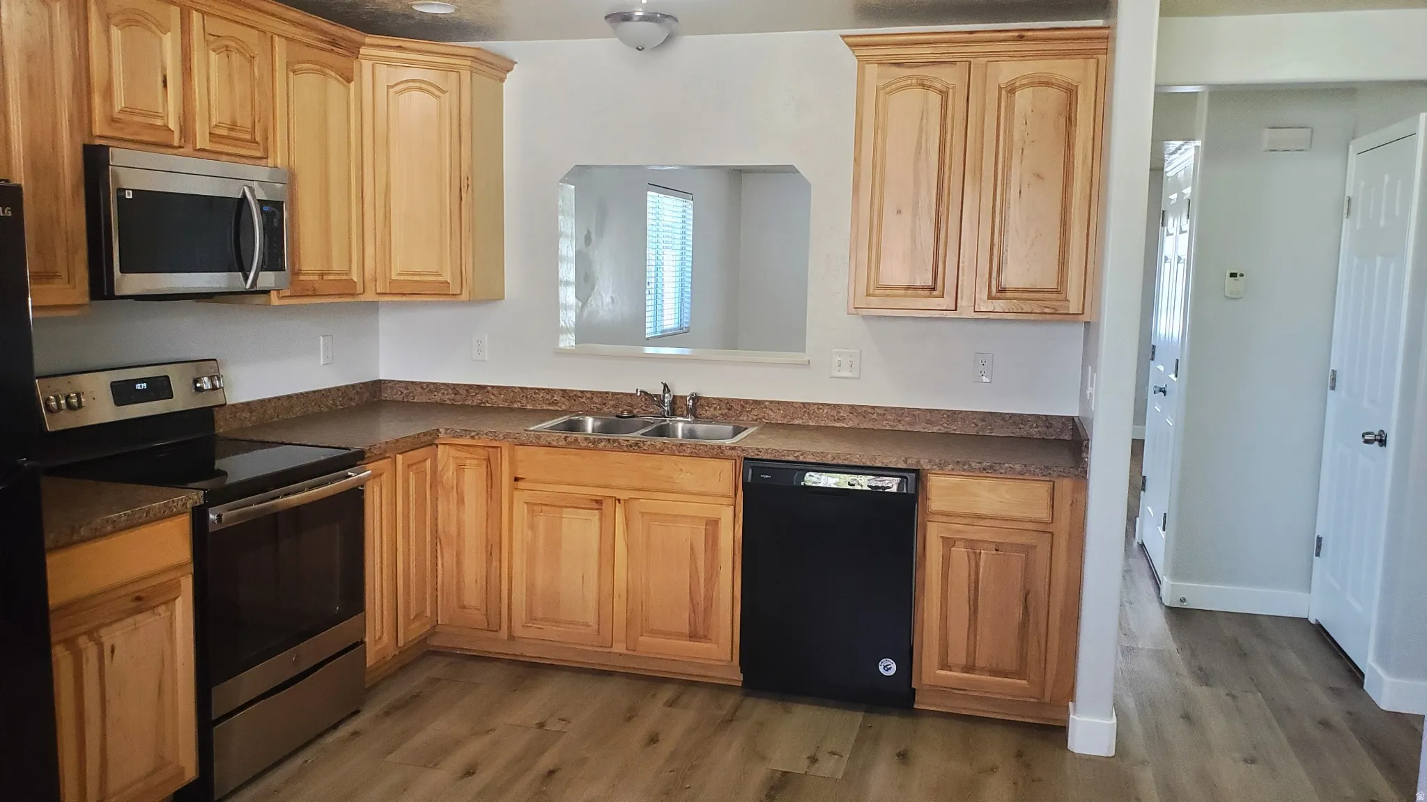 L-shaped kitchen featuring wood cabinetry, granite-look countertops, and wood-finish flooring