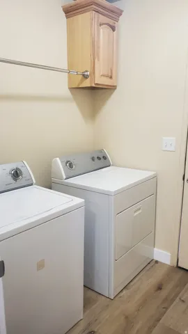 Laundry area featuring wood-finish flooring, a wall-mounted light wood cabinet with crown molding, and a chrome hanging rod