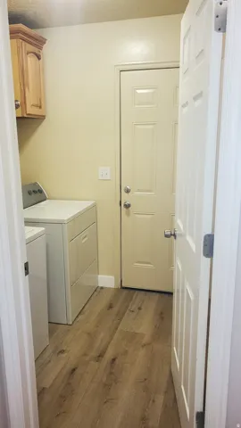Utility room featuring wood-finish flooring, light-toned walls, and a built-in wood-finish cabinet