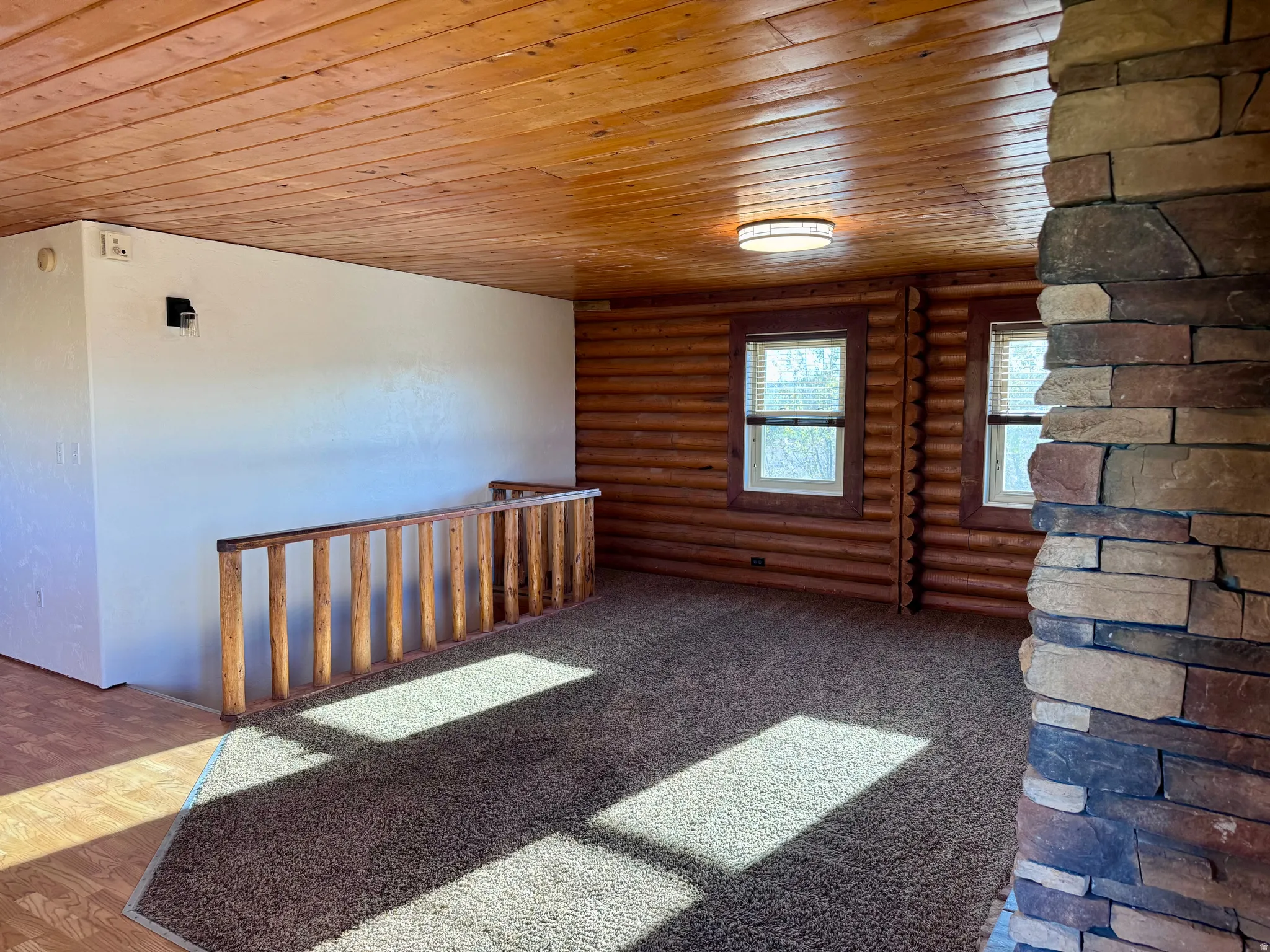 Room featuring a wood-panel ceiling, stone-clad architectural element, and wood-log walls
