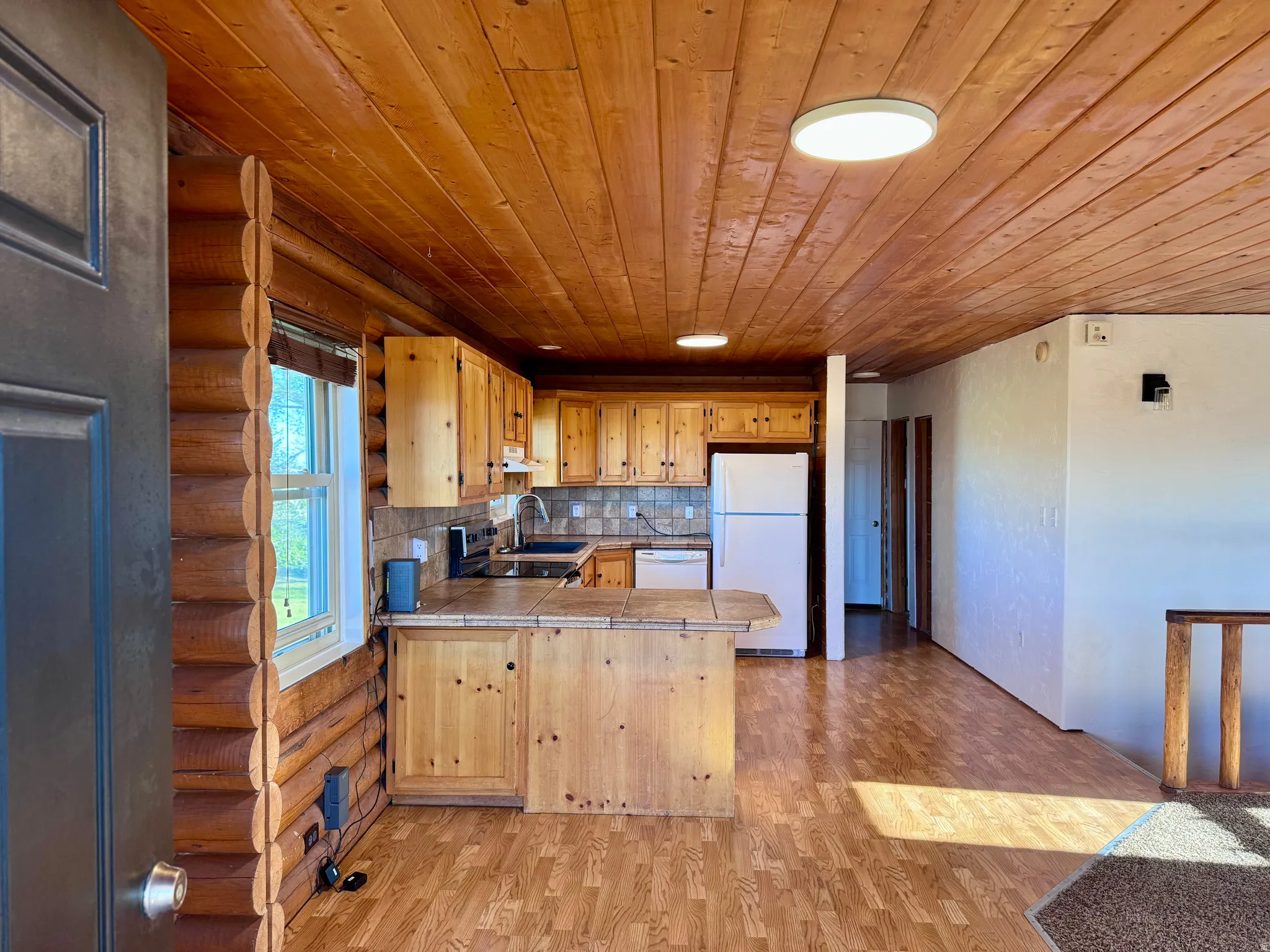 Open-concept living space featuring a kitchen with light wood cabinetry, tile countertops, and a stone-look backsplash